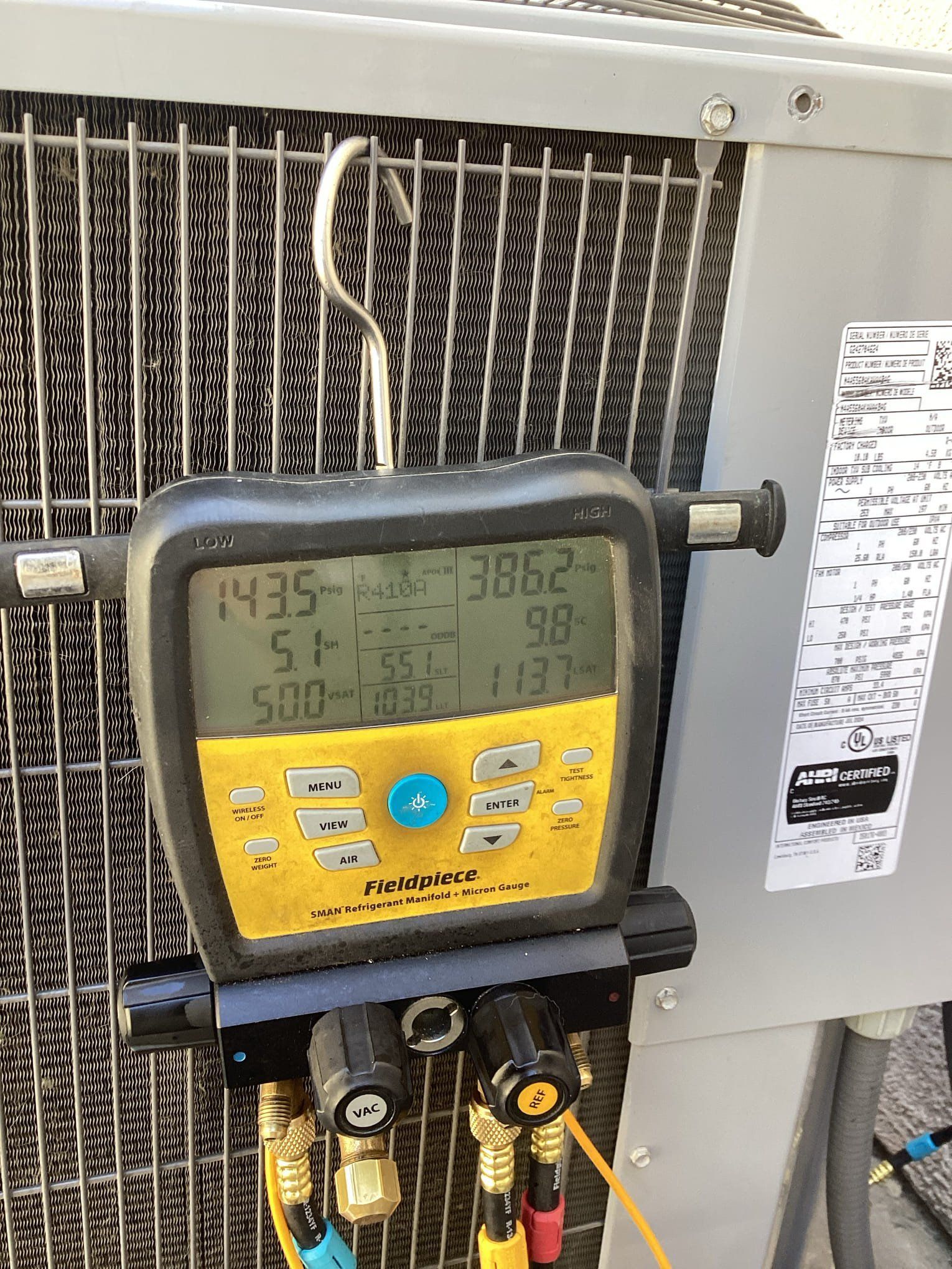 Digital HVAC gauge connected to an outdoor unit, displaying pressure readings.
