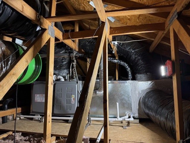 Attic with HVAC system, ductwork, wooden supports, and insulation.