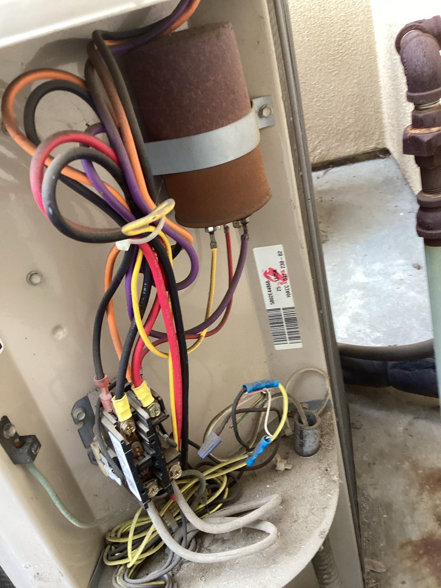 Open AC unit electrical components: capacitor, wires of various colors, terminal block, and wiring connections.