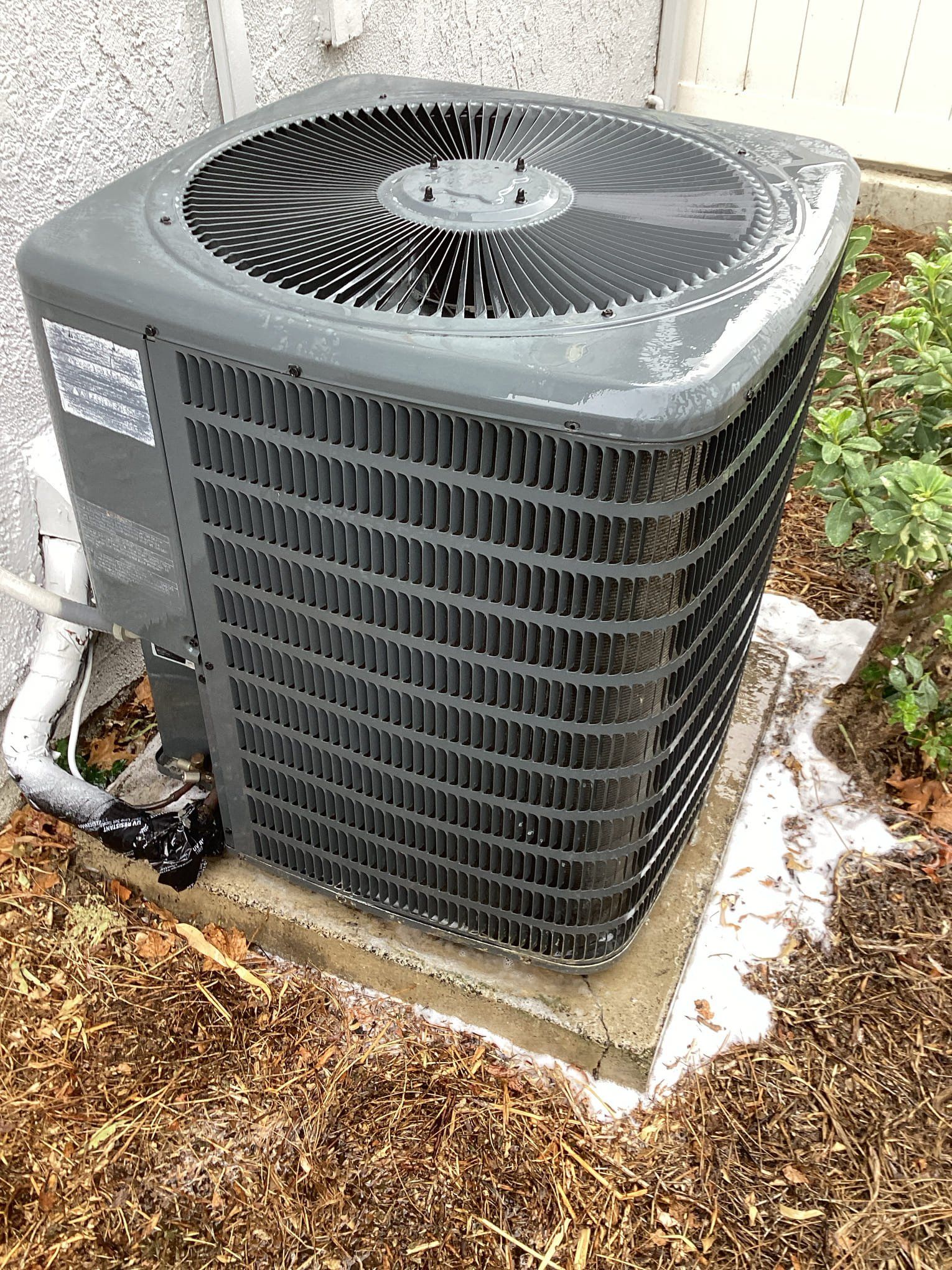 Outdoor air conditioning unit with black fins and fan. Gray casing, on concrete base with foam around it.