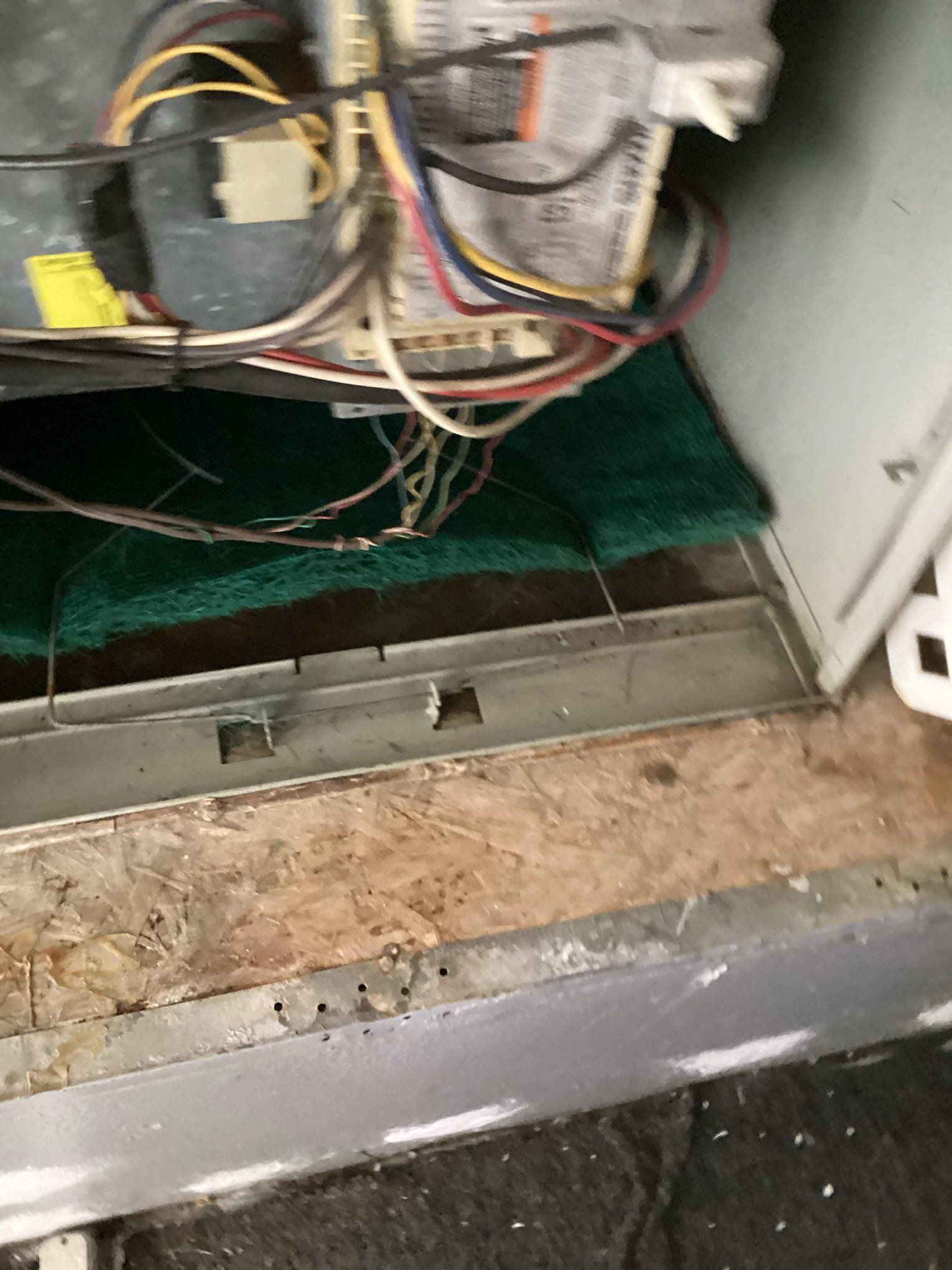 Interior view of a furnace showing wiring, a green filter, and exposed wood and metal.