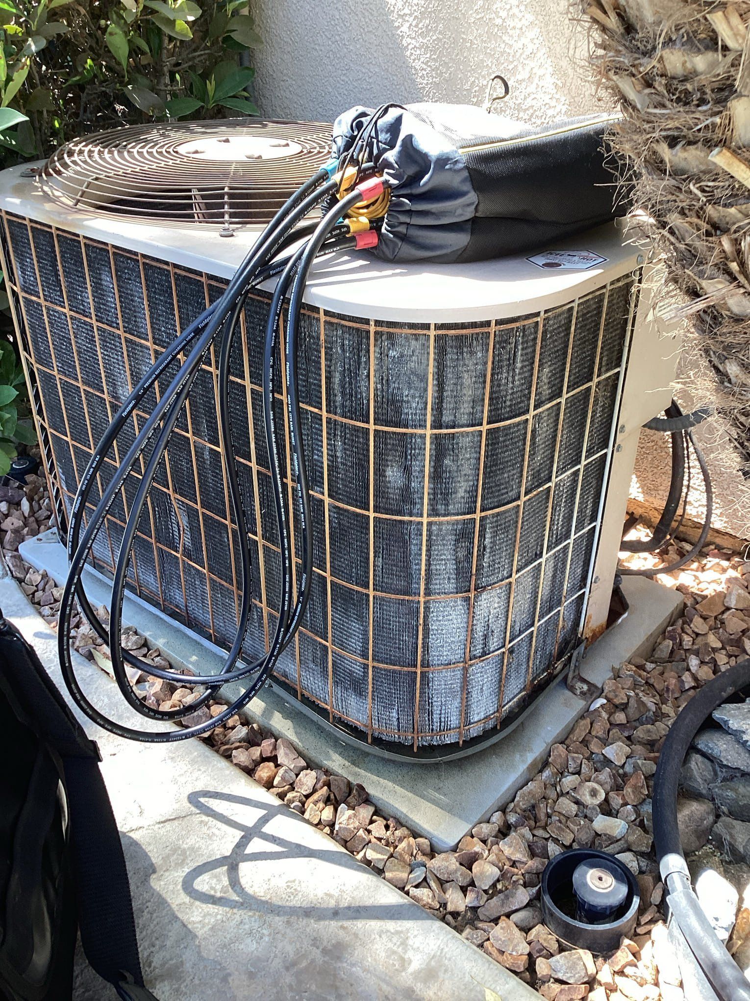 Air conditioning unit with protective cover, wires, and a concrete base, set on rocks.