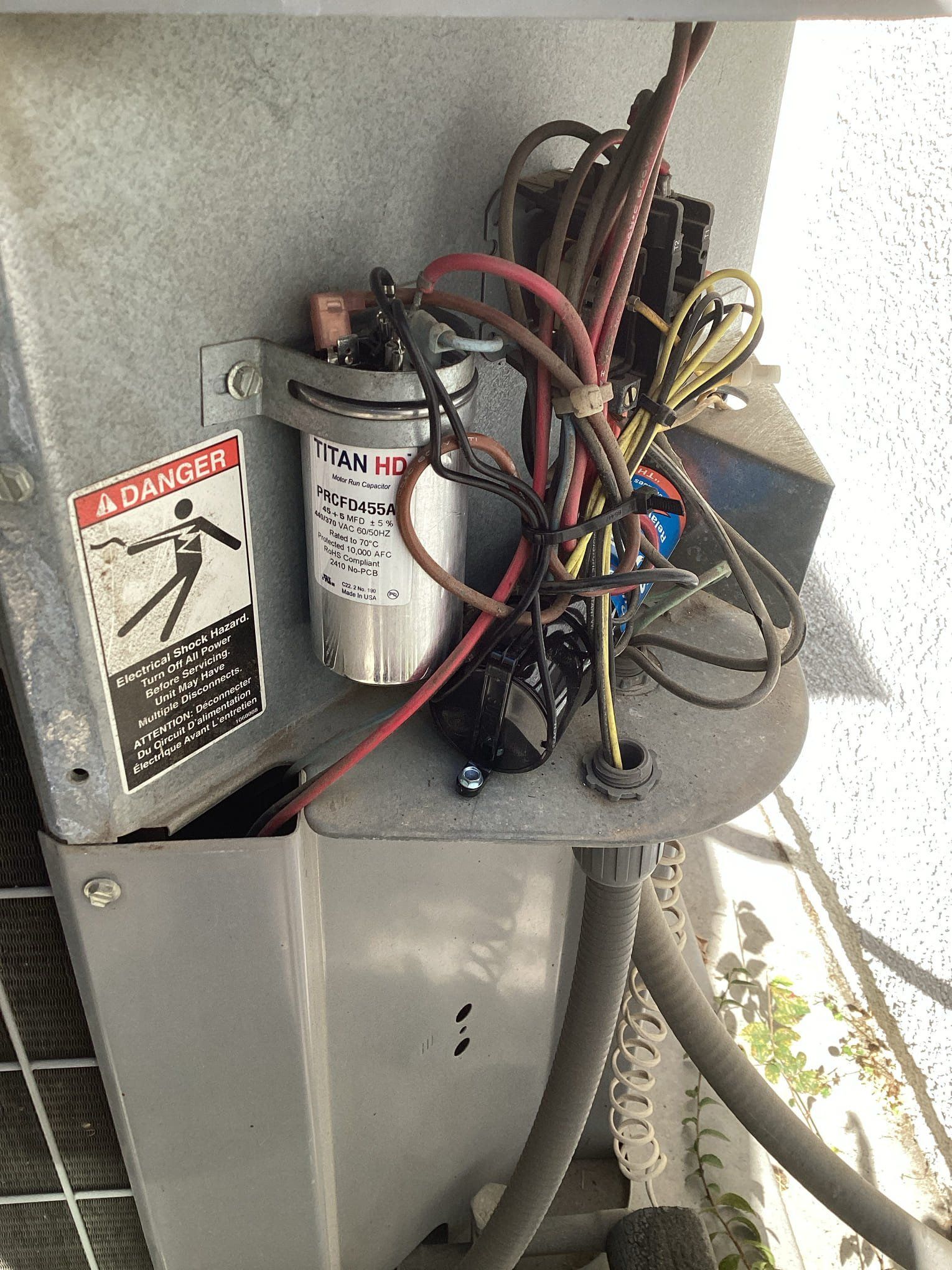 Air conditioning unit's electrical components: capacitor, wires, and warning label.