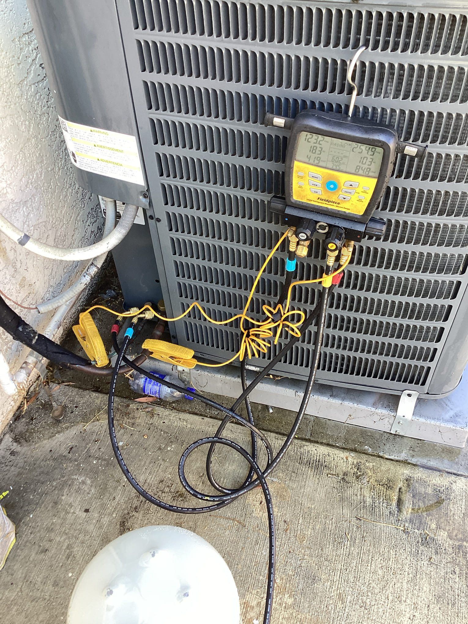 AC unit with gauges attached, measuring pressure. Hoses and equipment on the ground.