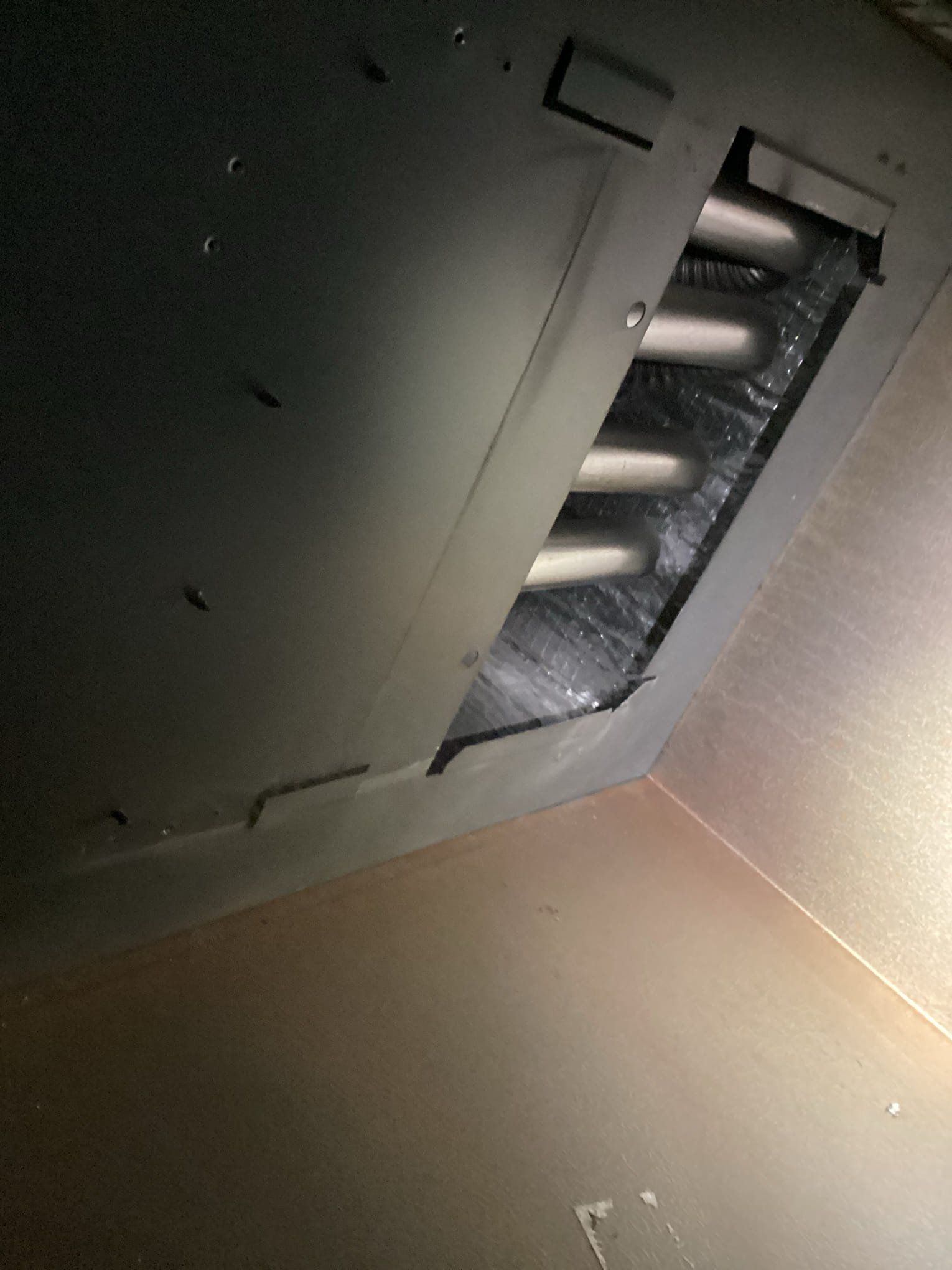 View inside a metallic rectangular air duct, revealing a series of cylindrical objects, possibly light fixtures or tubes.