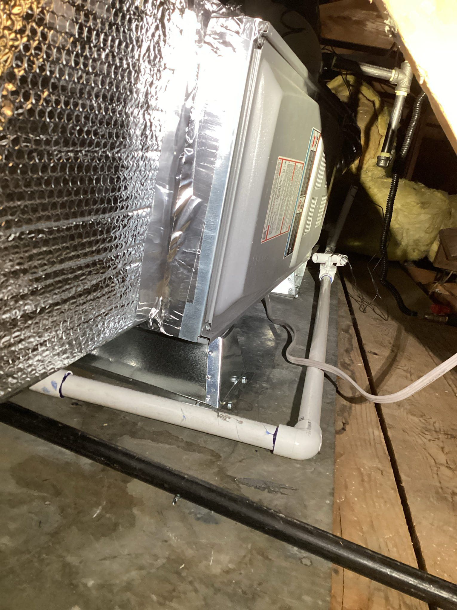 HVAC unit in an attic with insulated ductwork and PVC drain pipe.