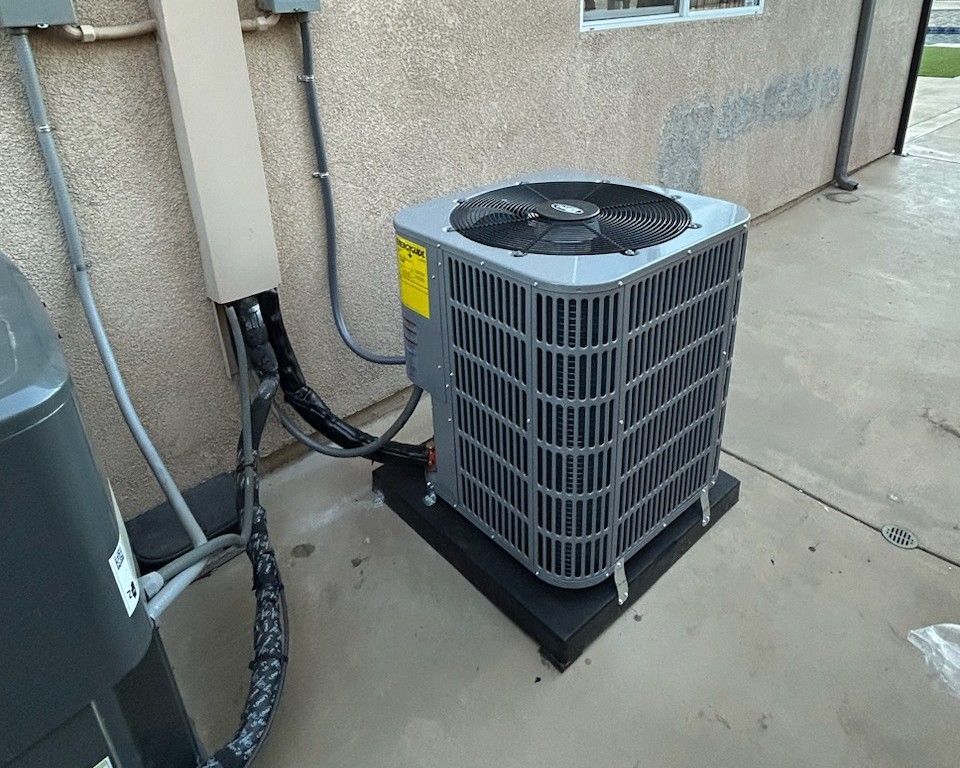 Air conditioning unit on a black pad outside a building next to electrical components.