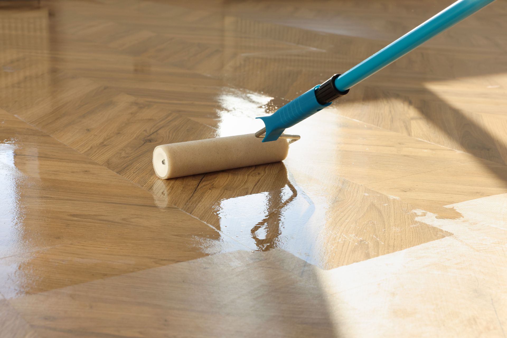 Applying sealant to a wooden parquet floor with a blue handled roller.