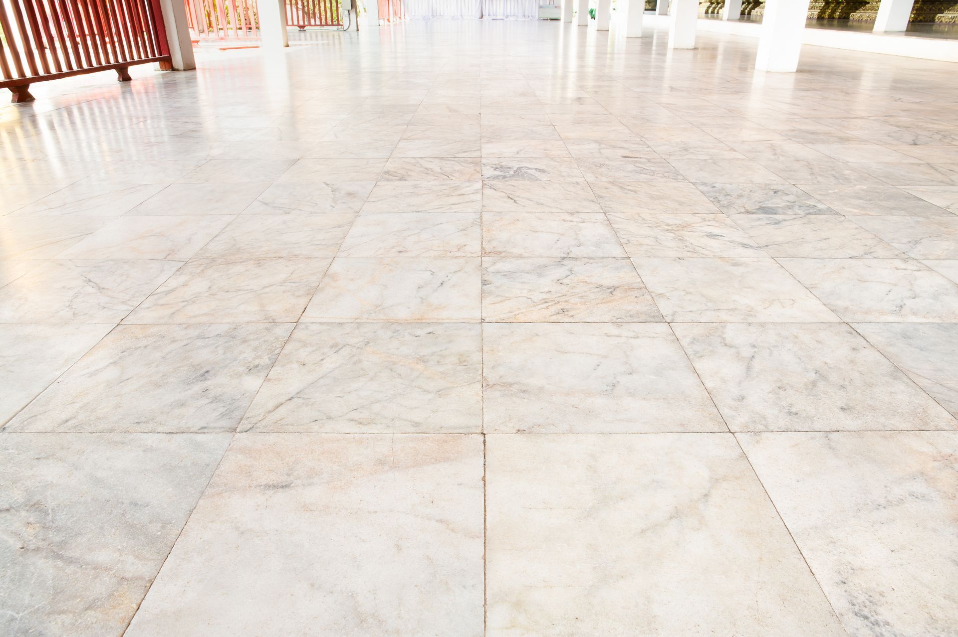 Marble tiled floor, light gray with veining, leading toward a red railing and white pillars.