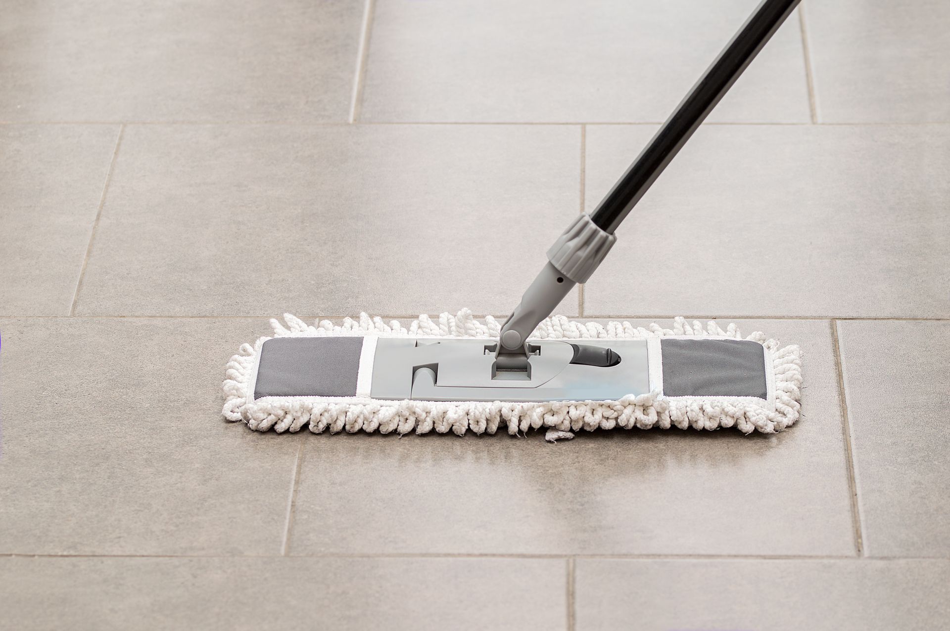 A microfiber dust mop gliding across a large-format gray tile floor with visible grout lines