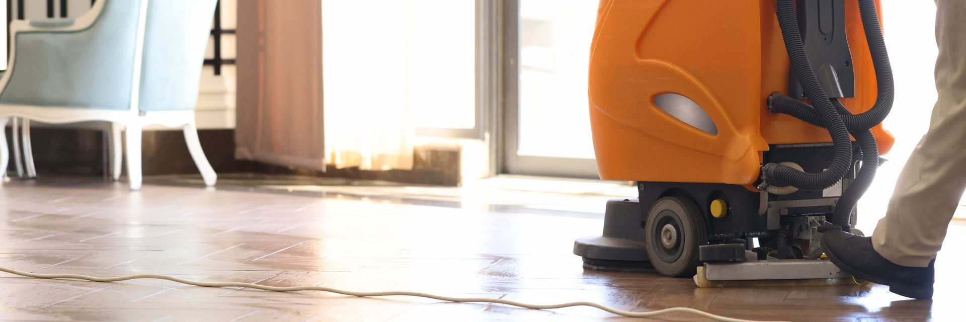 A person operates an orange floor cleaning machine on a shiny wooden floor.