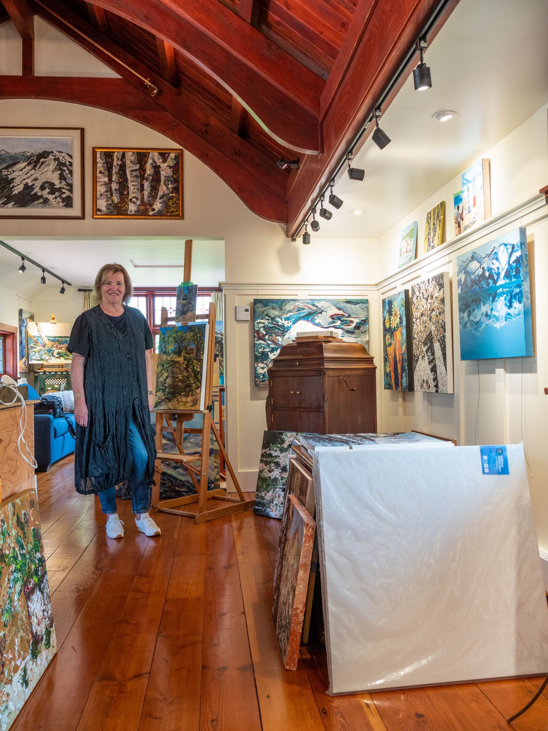 Hilary Kerr standing in her studio with rustic beams and a traditional studio design with her art hung on the wall. 