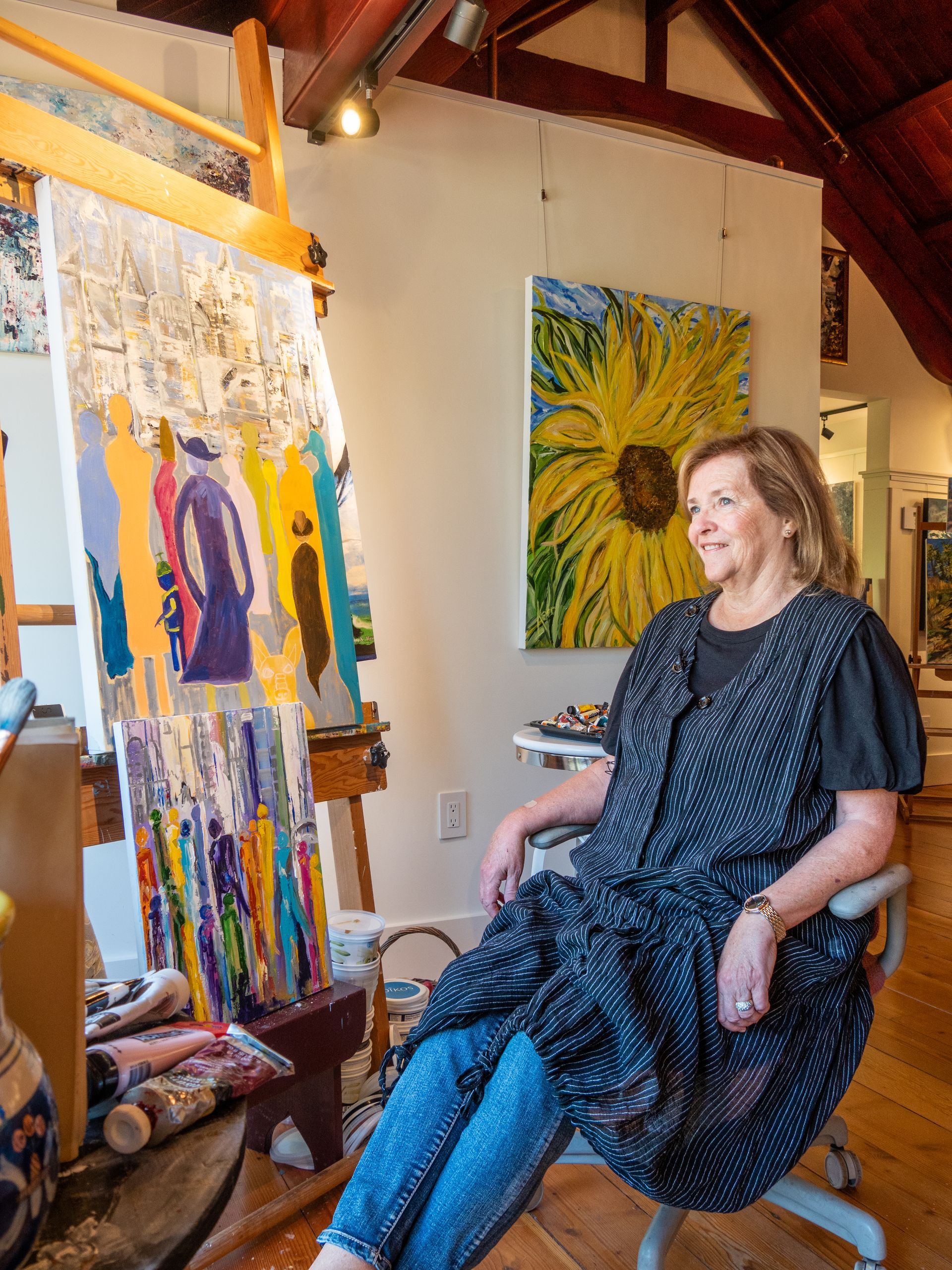 Hilary Kerr sitting down, smiling, looking outside while she sits next to a piece of art she is working on. 