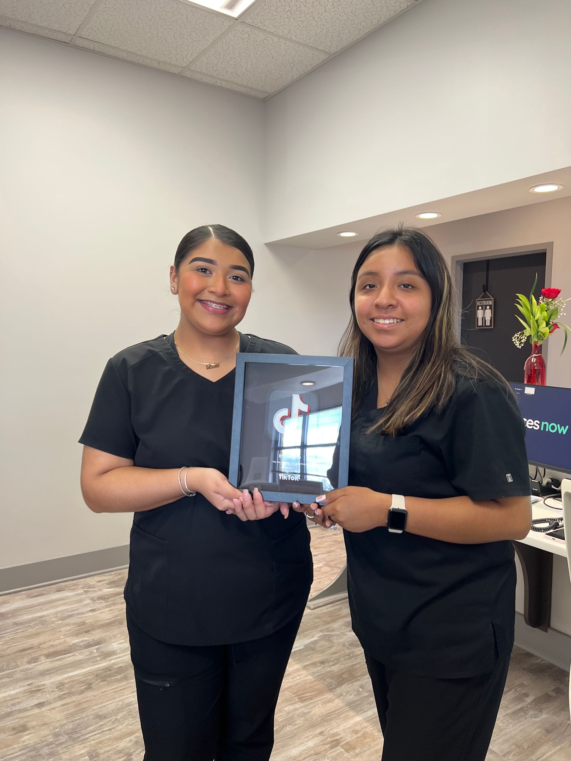Two women in black scrubs are holding a tablet