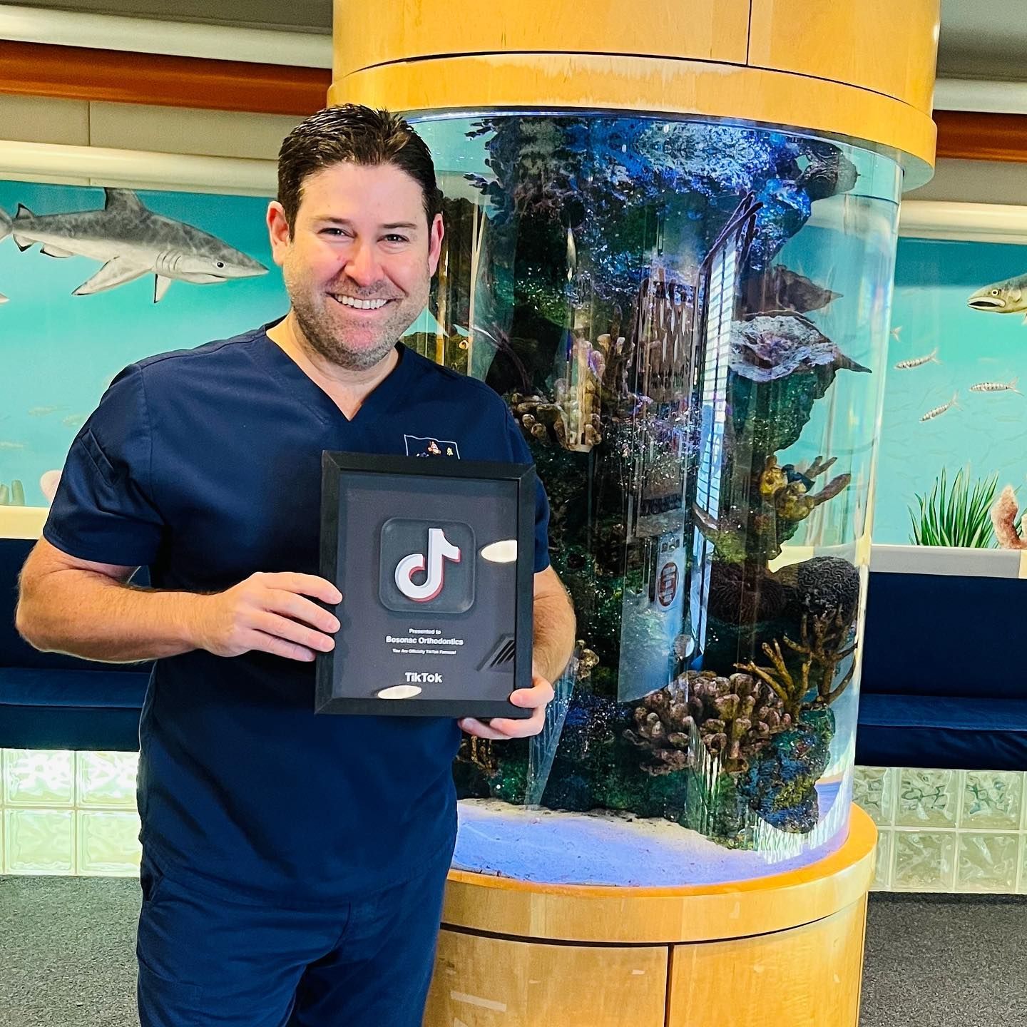 A man is standing in front of an aquarium holding a tik tok sign.