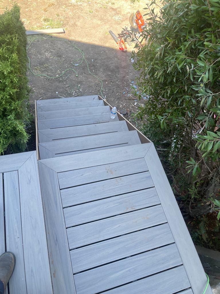 Composite deck stairs leading down from a deck, surrounded by greenery.