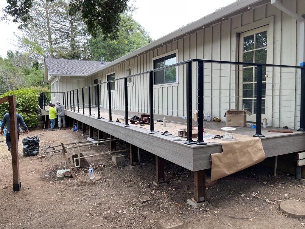 Deck construction next to a house with black railings, workers, and materials.