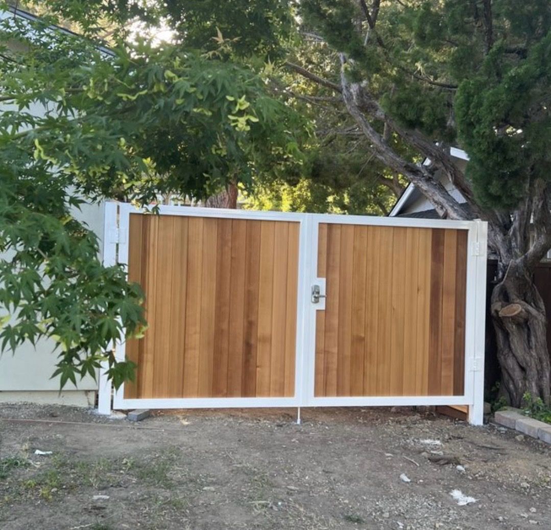 A white-framed double gate with vertical wooden slats stands outdoors in front of a tree.