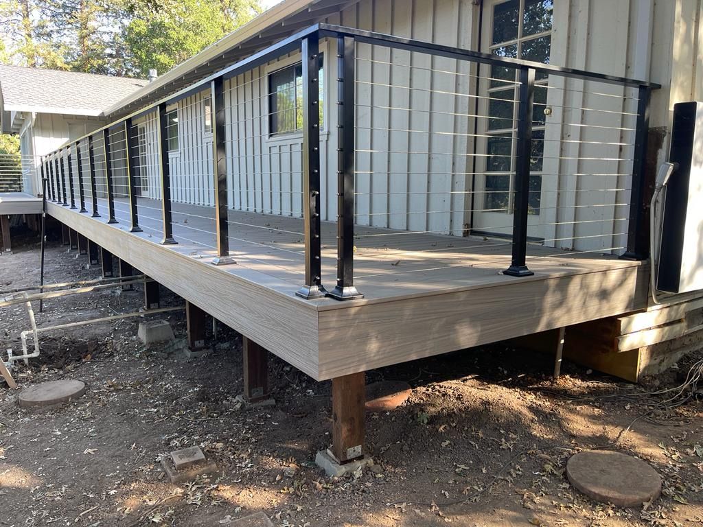 A newly built wooden deck with black railing extends from a white house.