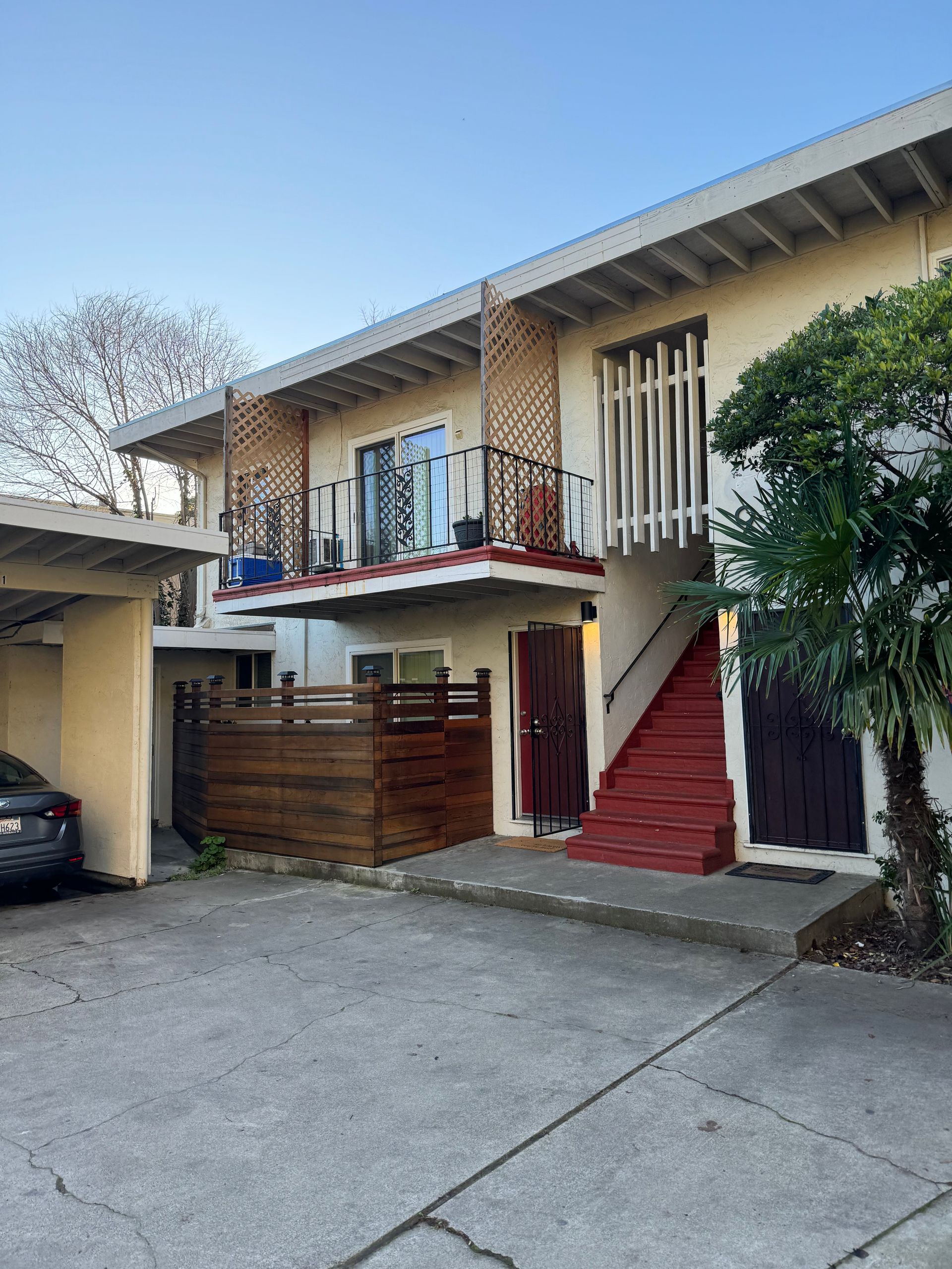 Two-story apartment building with balconies, wood fence, covered parking. Exterior is beige with red accents.