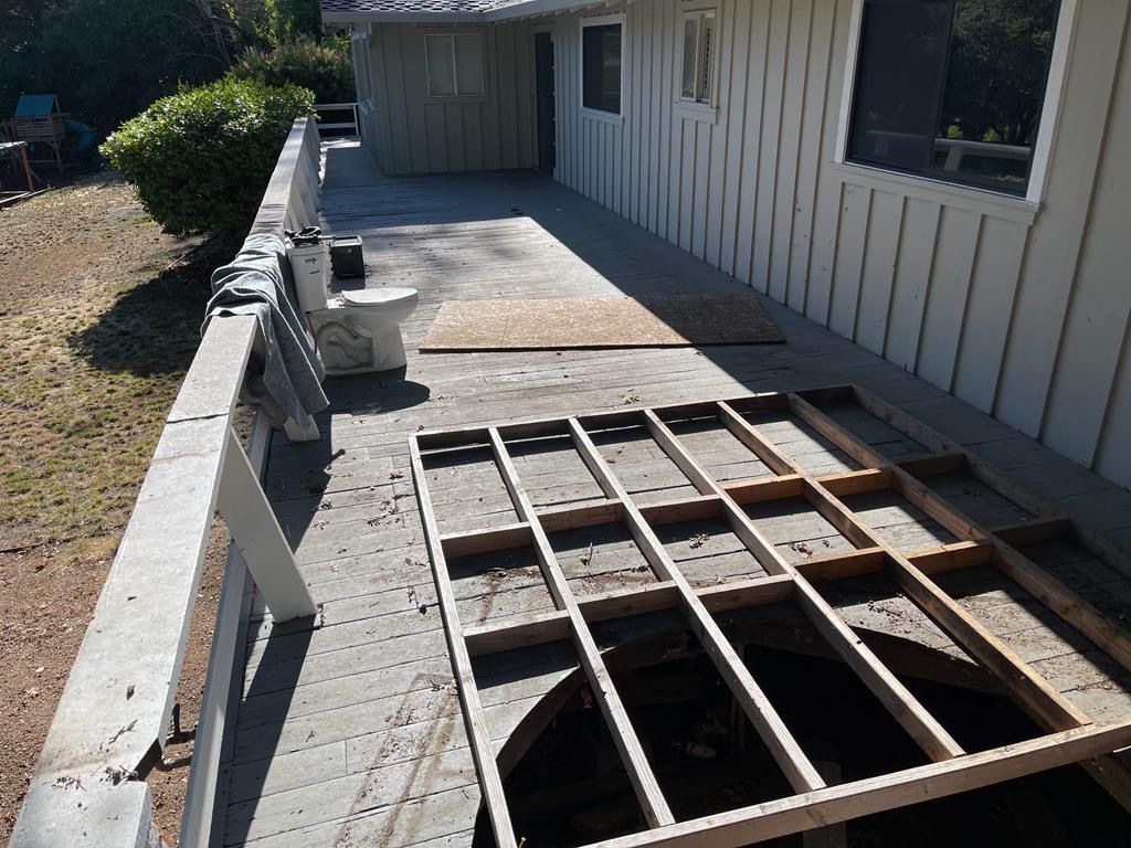 Deck under renovation, exposing wood framing. Parts of deck boards removed; house and railing visible.
