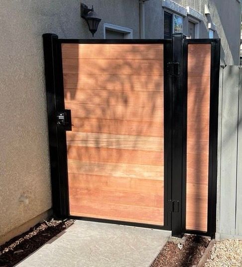 A modern gate with horizontal wood planks framed in black metal, installed between a stucco wall.
