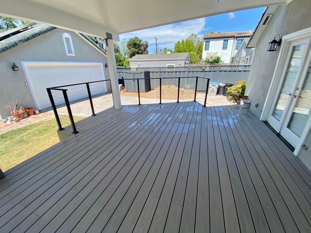 Wooden deck with black railing, overlooking a backyard with a garage.