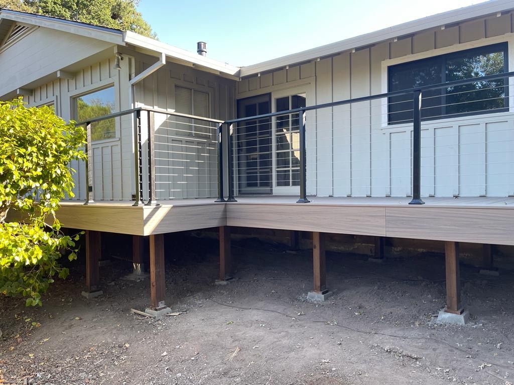 A raised wooden deck with a black metal railing attached to a light-colored, vertical-sided house.