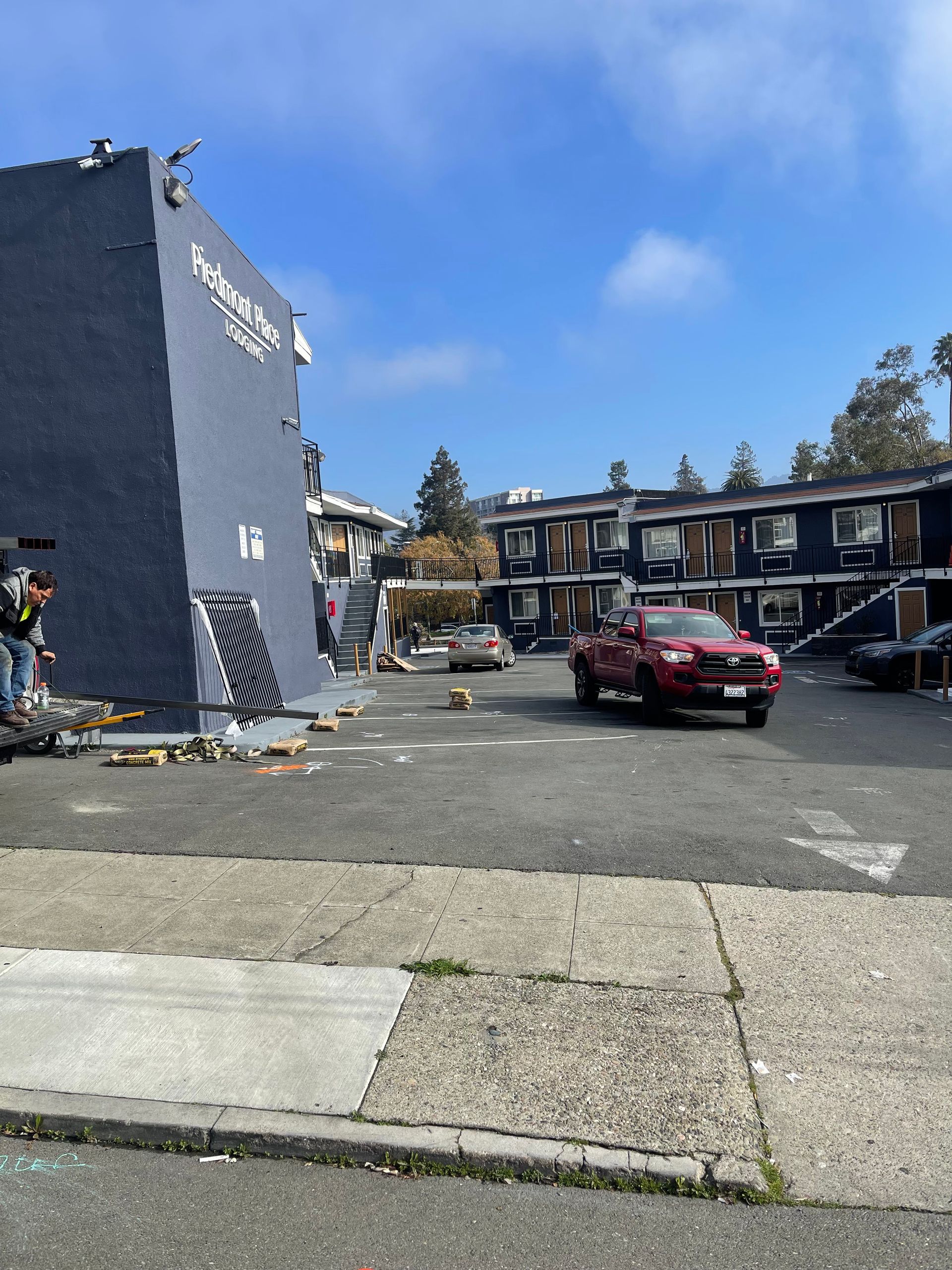 A blue motel exterior with a red pickup truck parked in the paved lot under a clear sky.