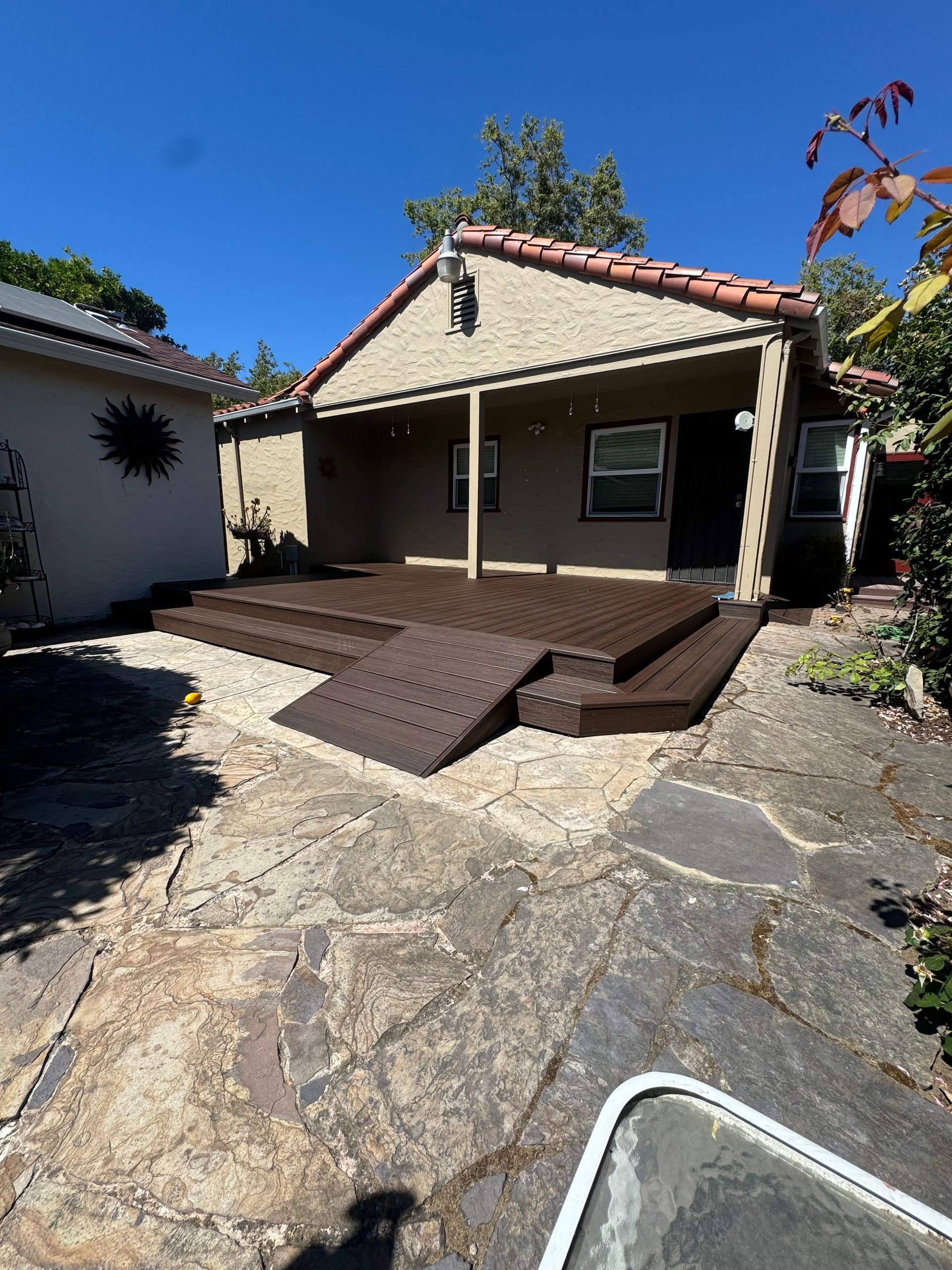 A brown composite deck with a ramp attached to the back of a house with a tile roof.