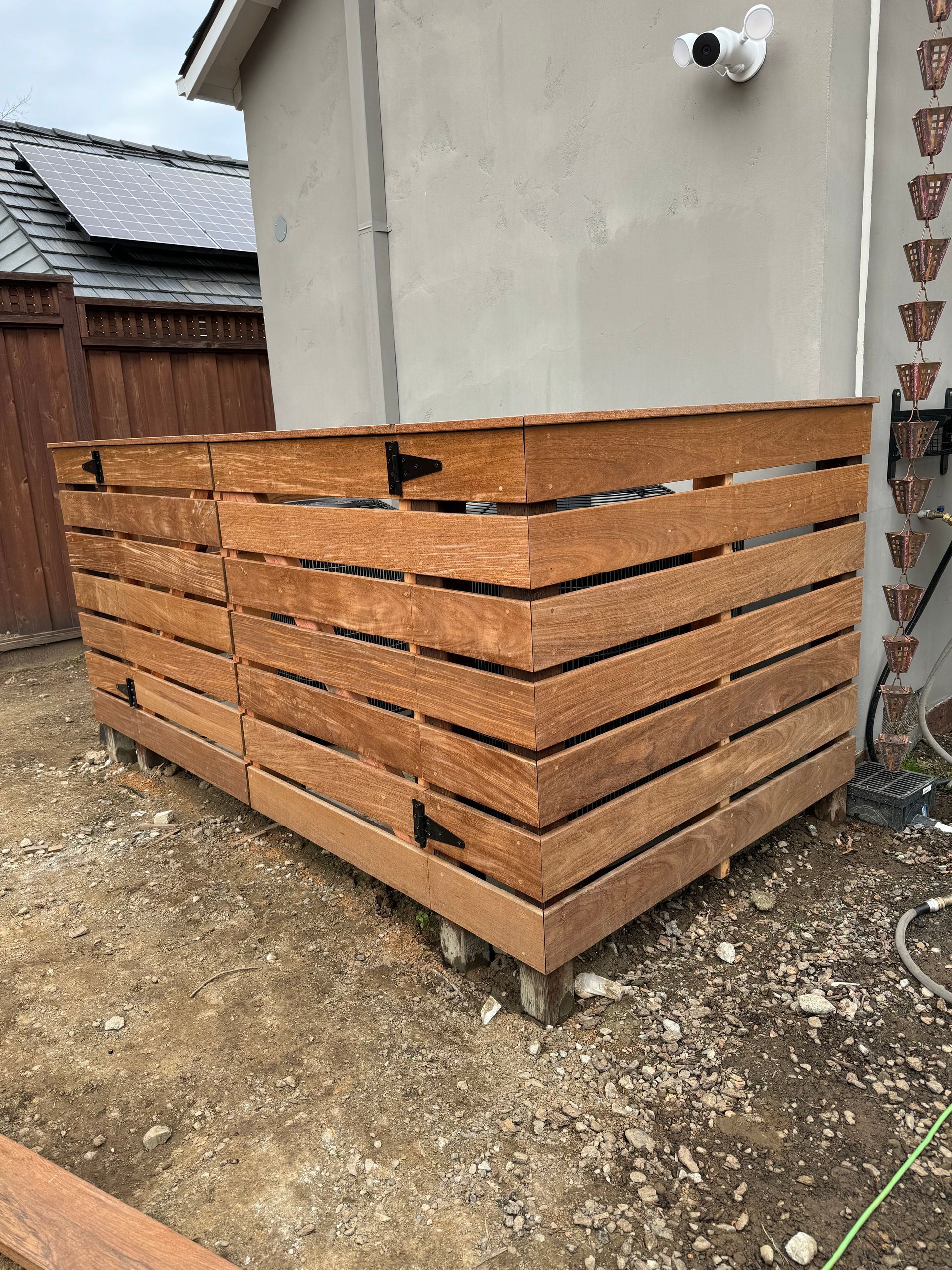Wooden air conditioner enclosure next to a light gray building. The enclosure has horizontal slats and is brown.