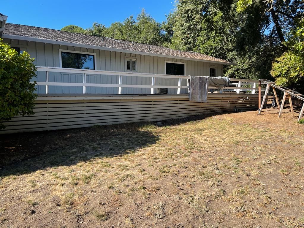 A light gray house with a wide white deck, white railing, and decorative lattice skirting sits on a dry, grassy yard.