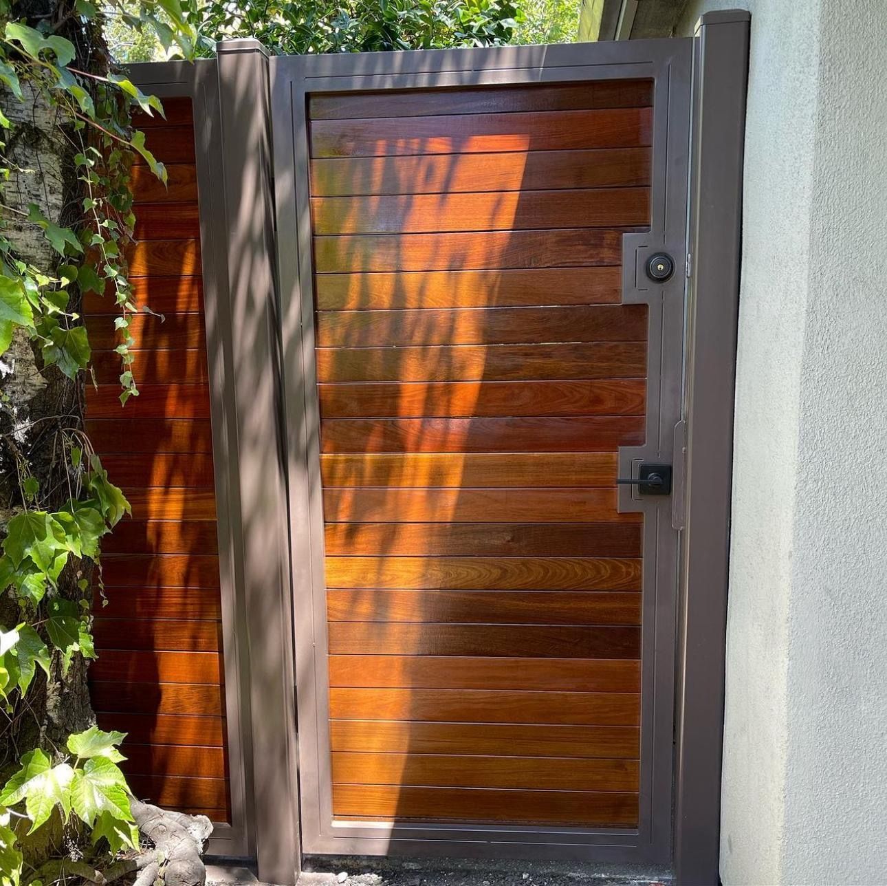 A rectangular wooden gate with horizontal planks and a dark metal frame, positioned next to a wall and ivy.
