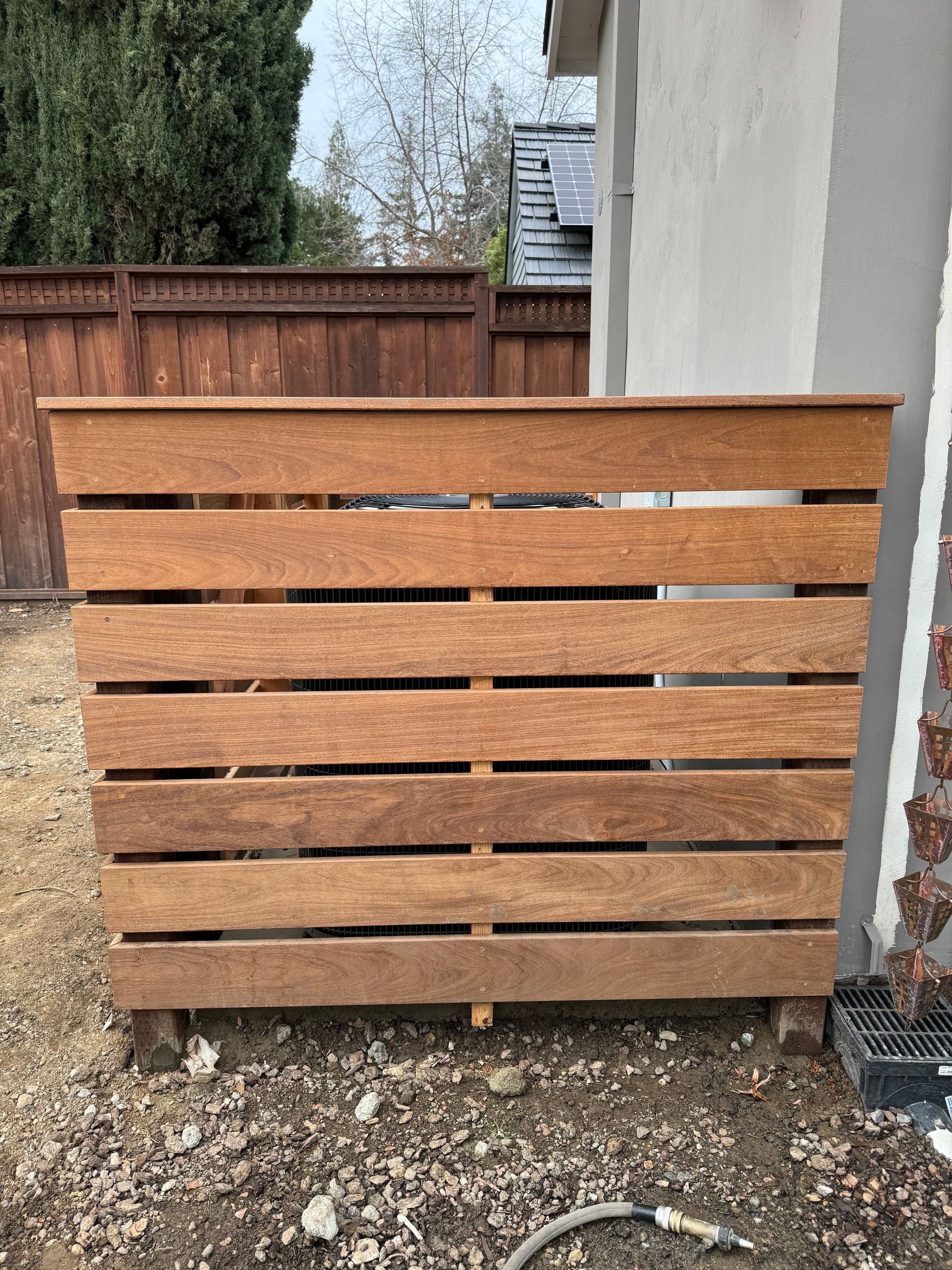 Wooden enclosure, likely for an AC unit, against a wall. Brown wood, horizontal slats. Outdoor setting.