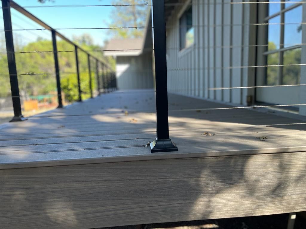 A low-angle view of a grey composite deck with black metal railing posts and horizontal cable wire infill.