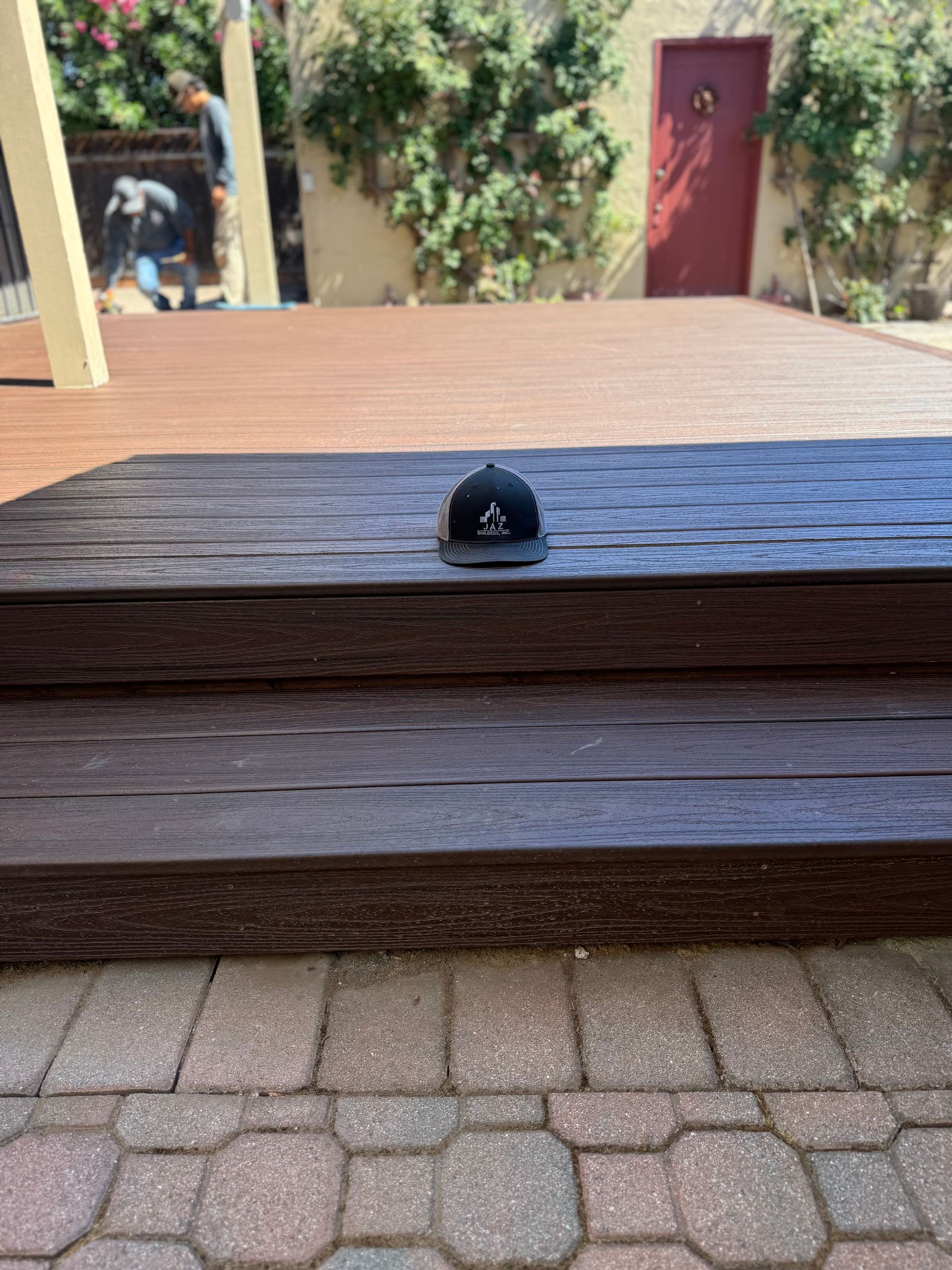 A black cap sits on wood steps leading to a deck; a person is visible in the background.