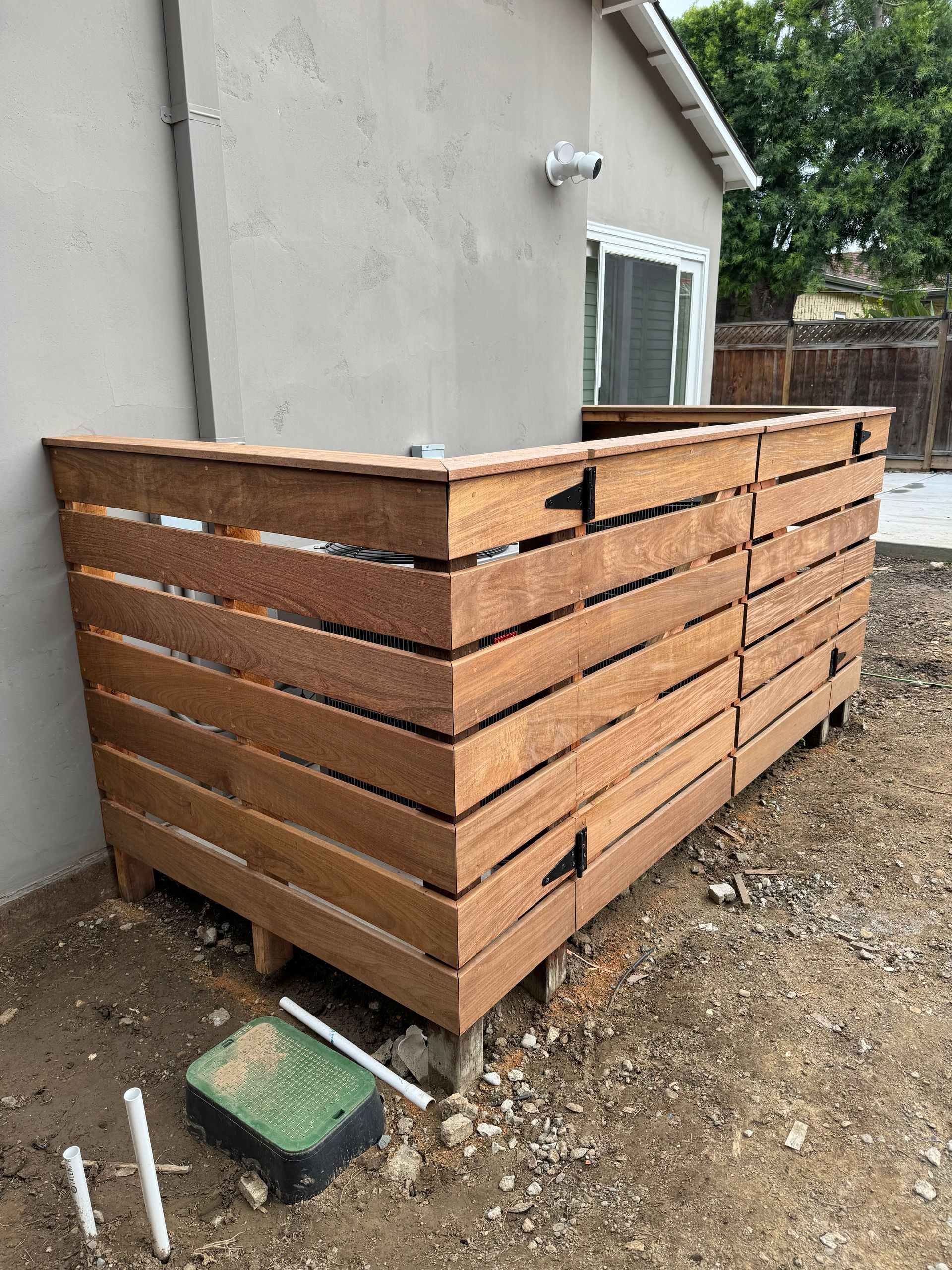 Wooden enclosure around an outdoor appliance, built against a stucco wall.