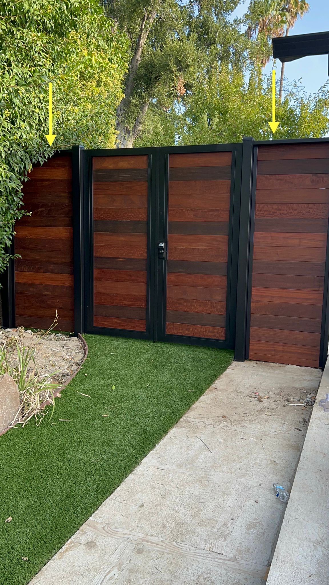 Modern wooden double gate with black metal framing set between a hedge.