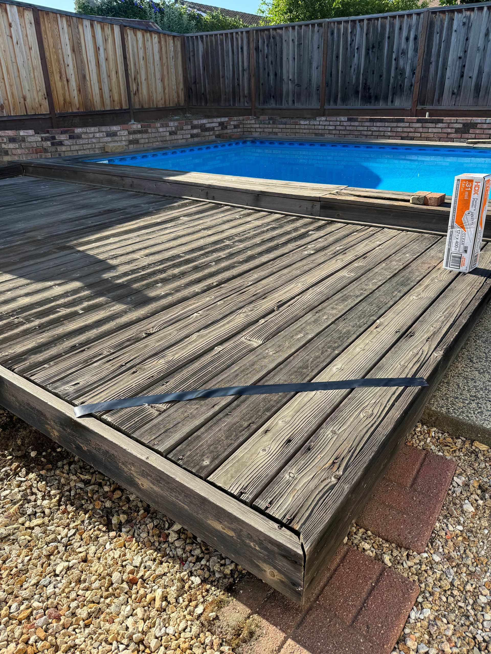 Wooden deck next to a pool with a blue cover, set in a backyard.