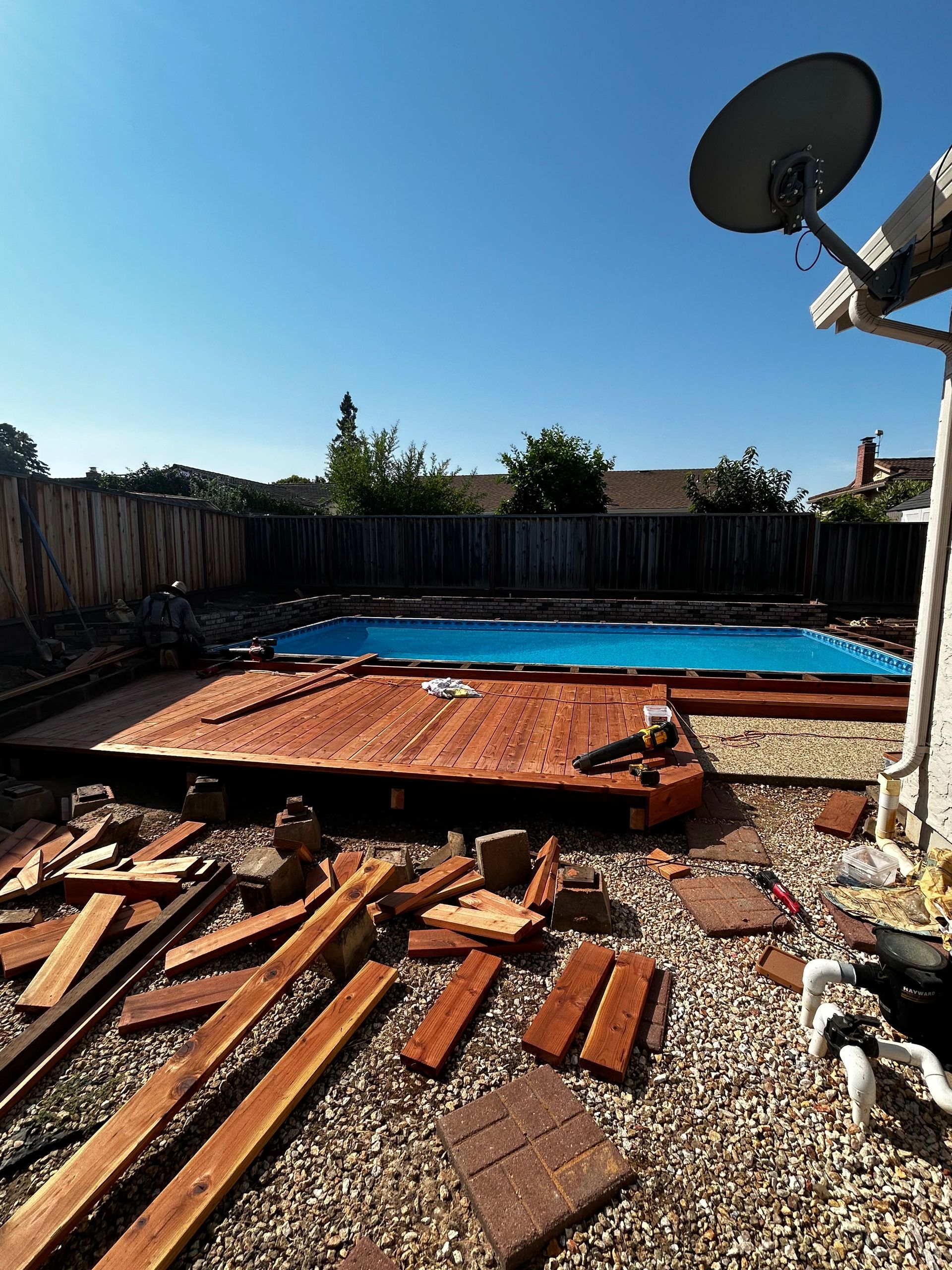 Backyard scene with a pool, gravel ground, and scattered wood. A dog is in the corner.