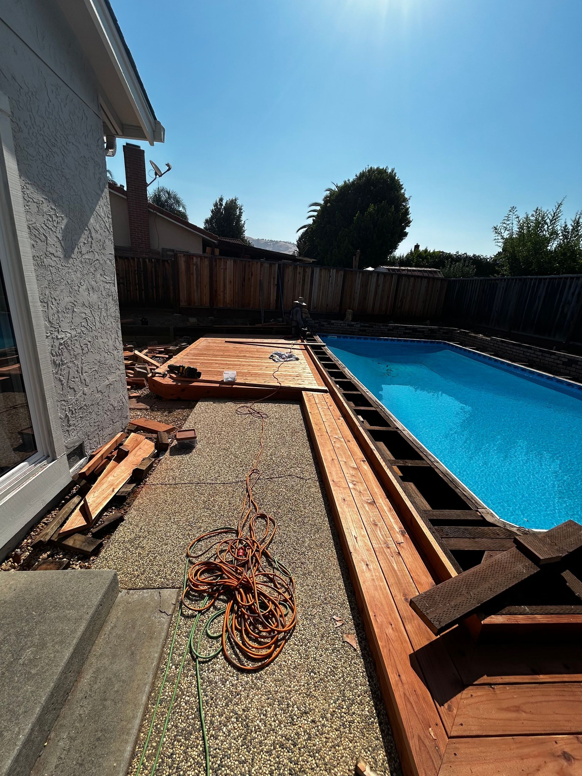 Backyard pool with a partially constructed wooden deck; sunny day.
