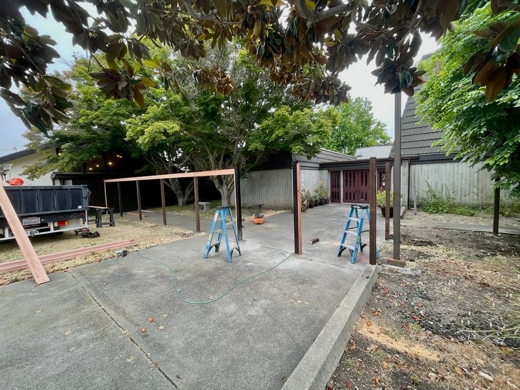 Construction site with wooden posts and ladders; concrete patio in front of a house.