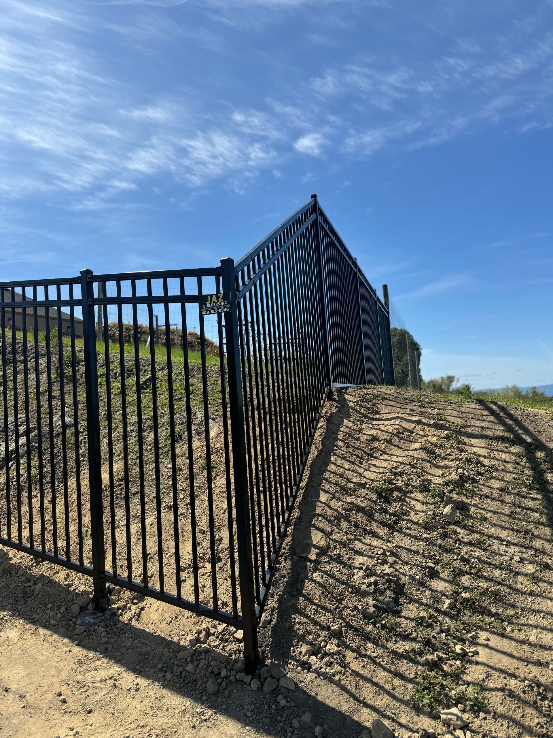 Black metal fence on a hillside under a blue sky.