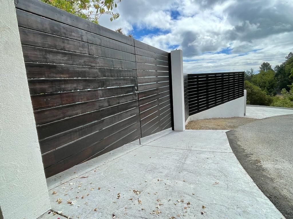 Dark wooden gate with concrete pillars and driveway.