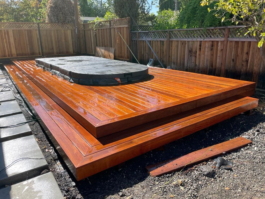 Wooden deck with a dark stone structure, surrounded by a wooden fence, outdoors.
