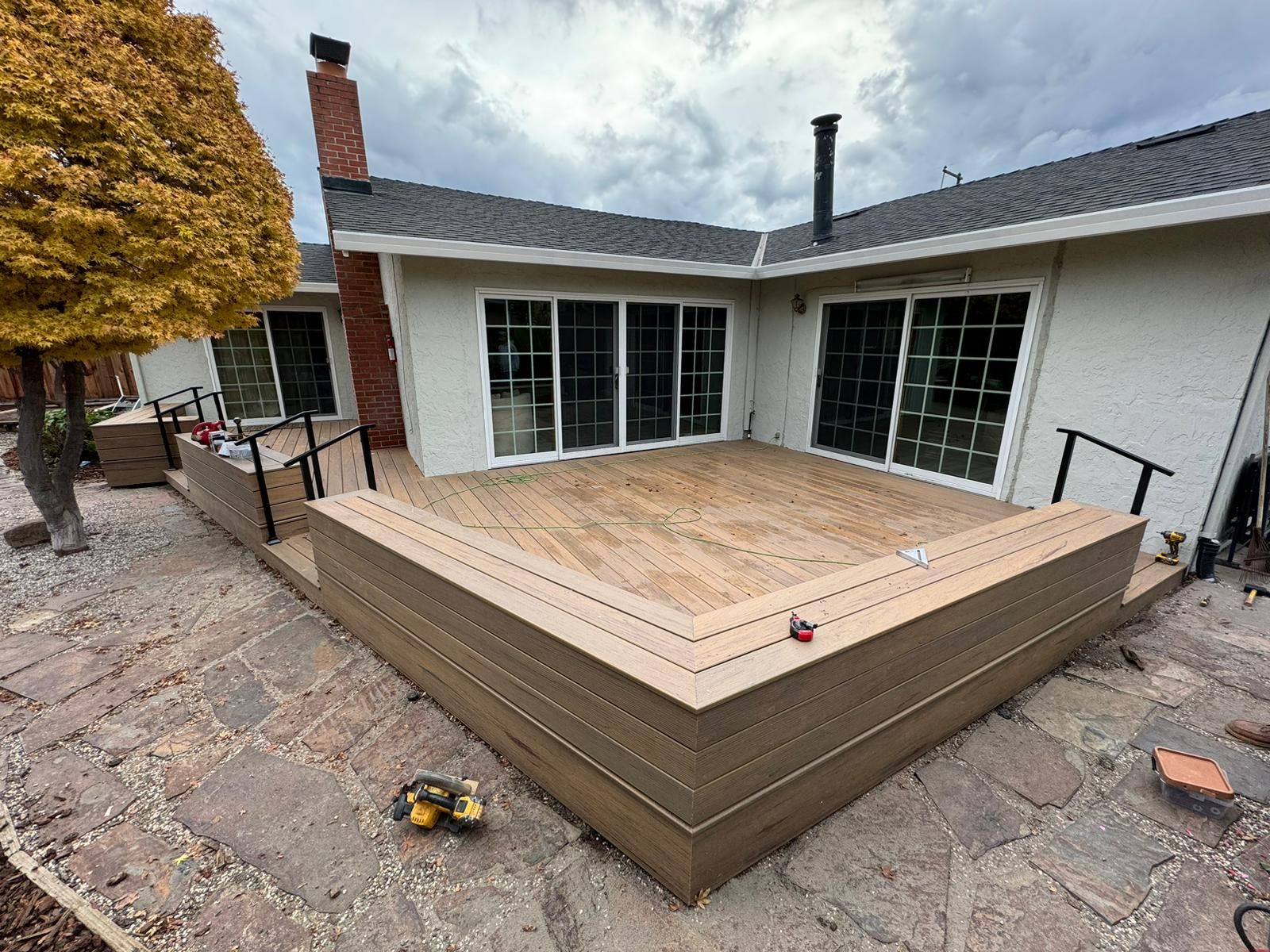 A newly constructed wooden deck with dark railings against a house with sliding glass doors. Overcast sky.