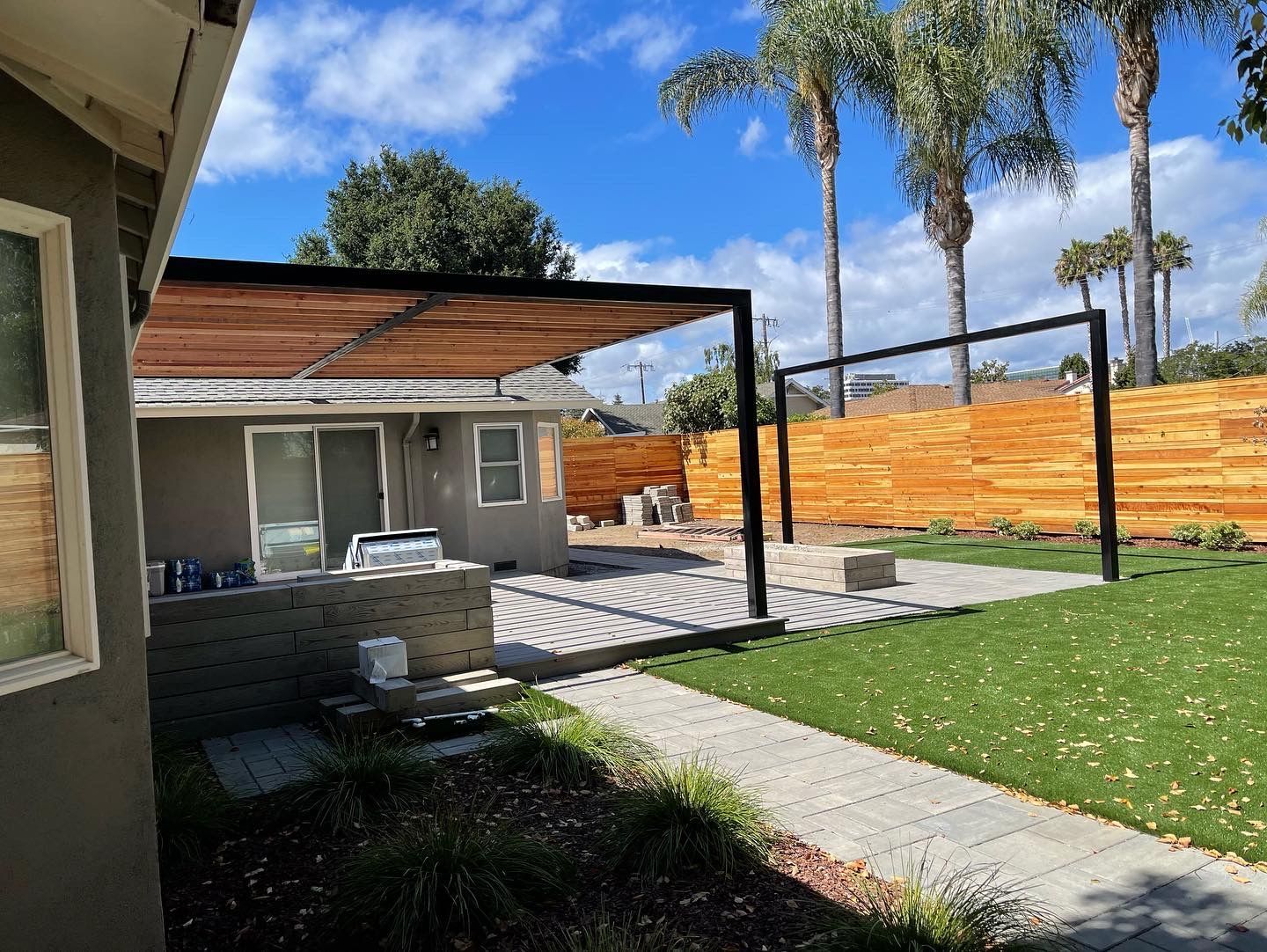 Patio with pergola, brickwork, green lawn, and wooden fence on a sunny day.