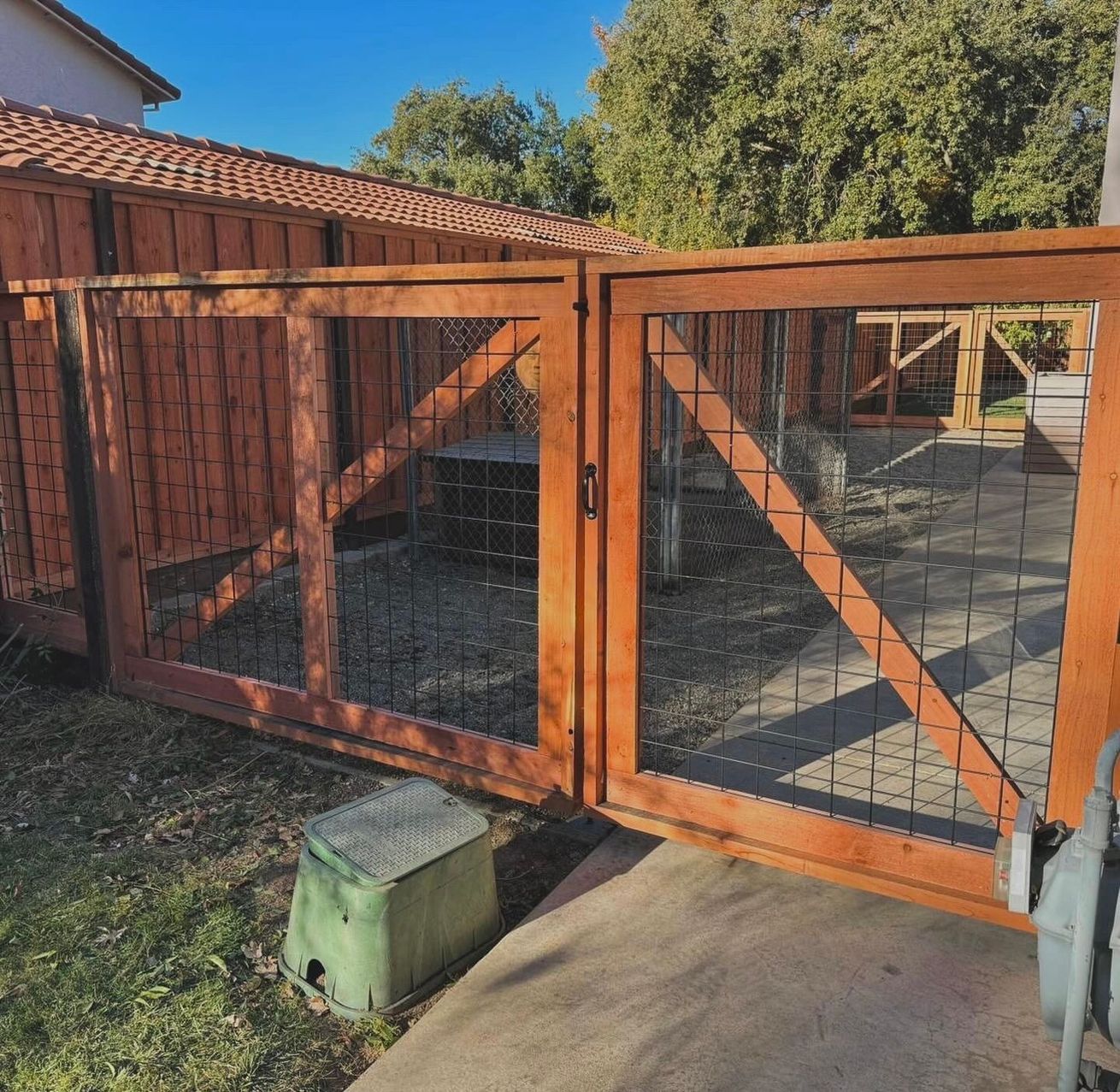Wooden gate with wire mesh, leading to an outdoor enclosure. Brown wood, green grass, and a concrete pathway.
