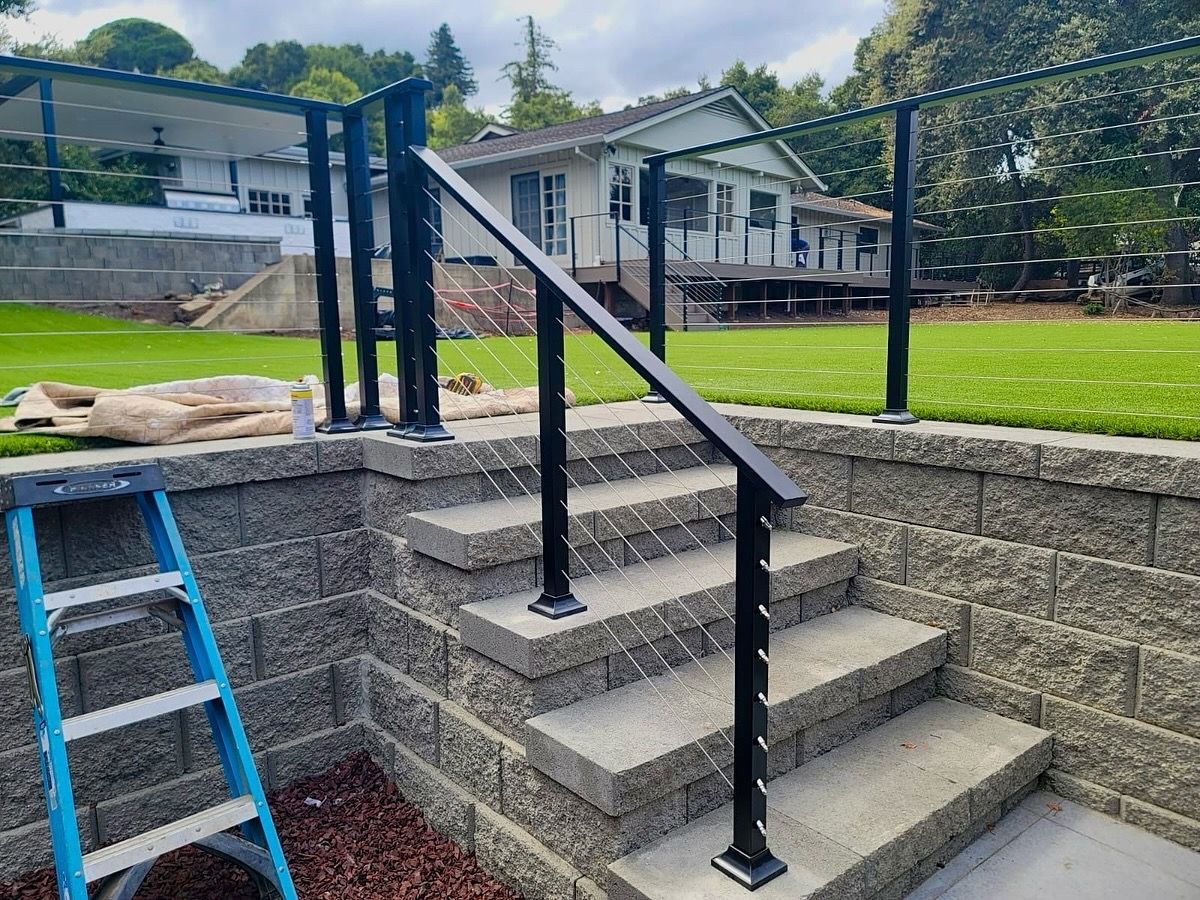 Wooden gate stained reddish-brown, with black hinges, handle, and latch, set against a wooden fence.