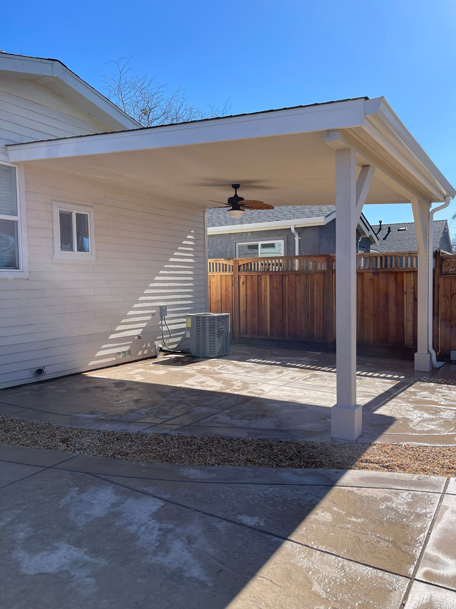 Backyard patio with a beige roof and support columns. A ceiling fan hangs from the roof.